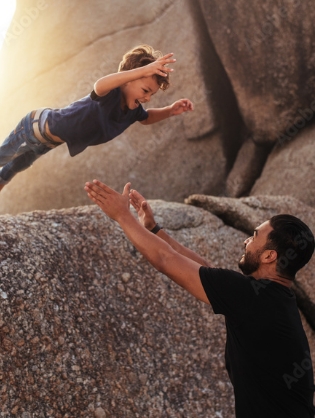 little boy leaping into his fathers arms from a big rock indicating trust.