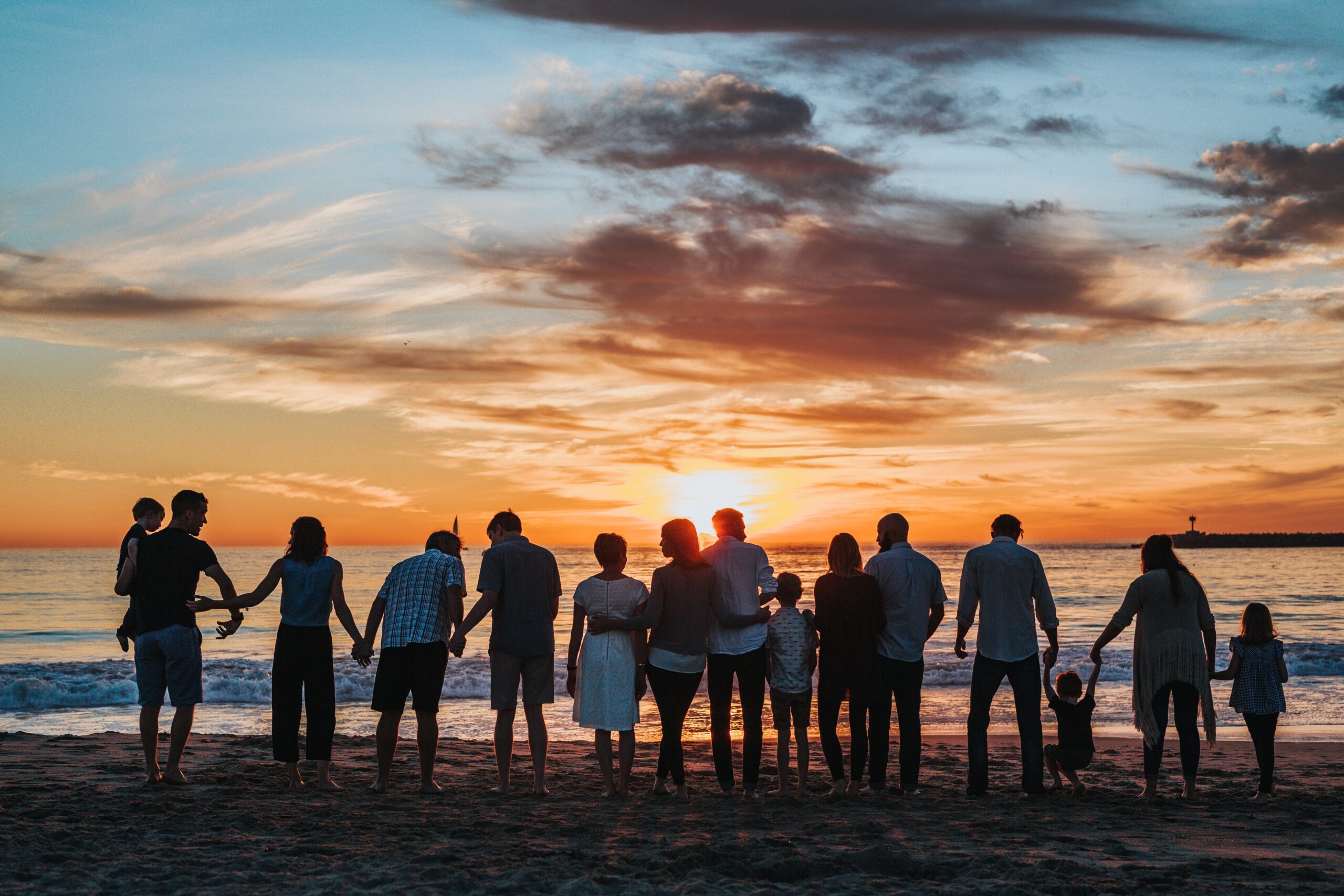 group mix of friends, family, kids standing on the shore enjoying sunset and fostering a sense of belonging.