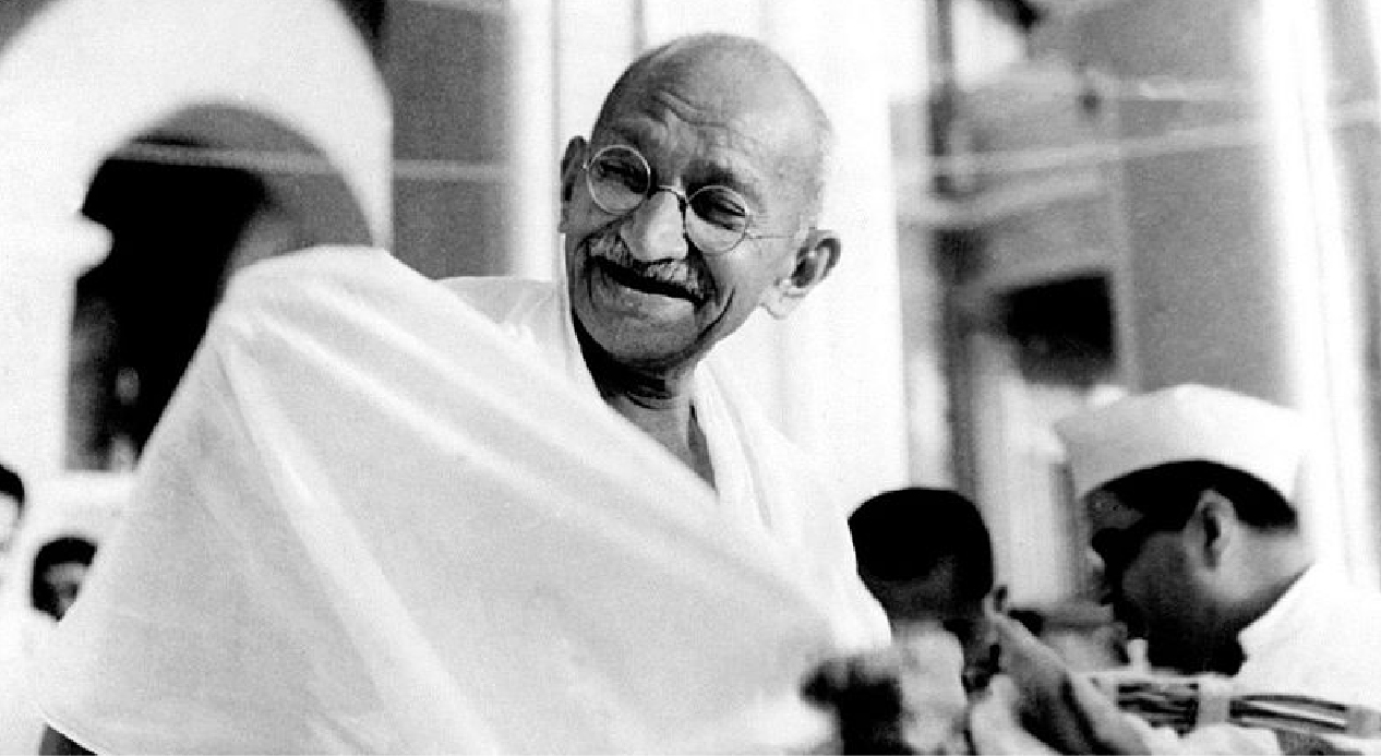 Mahatma Gandhi smiling with a few people standing behind him randomly, indicating inspiring them to be their best.