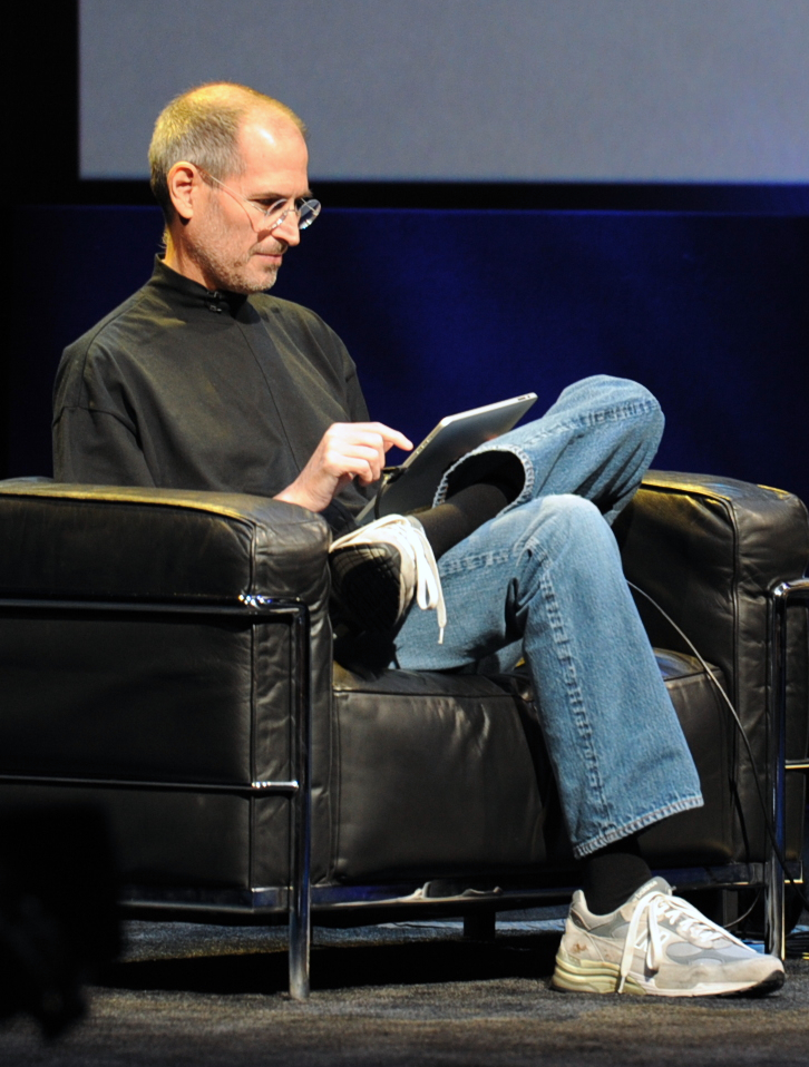 Steve Jobs sitting on a black sofa with ipad in his hands demonstrating it's okay to dream the impossible, as long as you are committed to relentlessly pursuing this dream.
