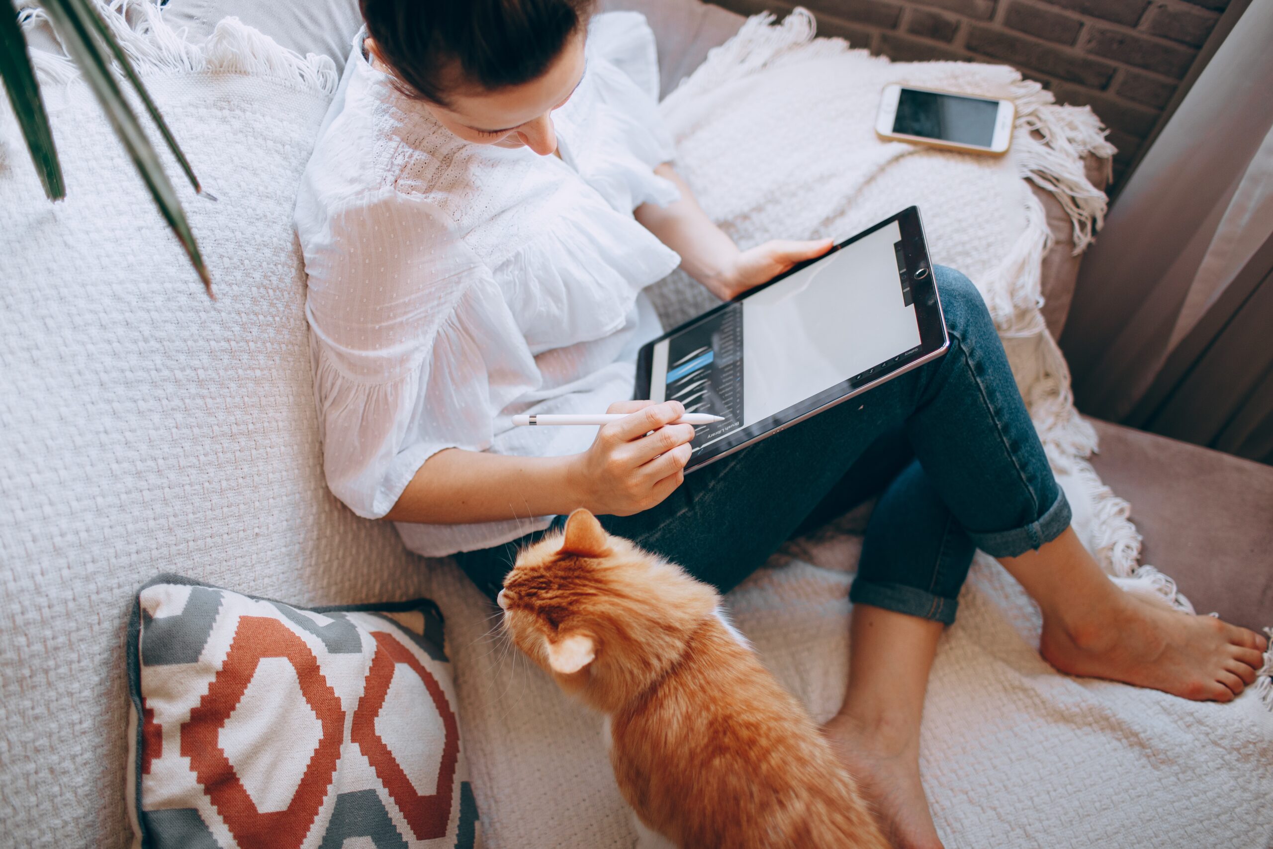 a girl sitting on sofa with her cat and working on ipad displaying working smarter, not harder.